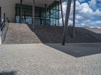 a person on a bike walking through a stone building entrance, in front of an enormous glass wall and stairs