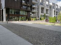 an asphalt street in front of apartment buildings and a bicycle path with cobblestone paved pavement