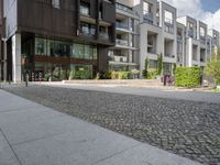 an asphalt street in front of apartment buildings and a bicycle path with cobblestone paved pavement