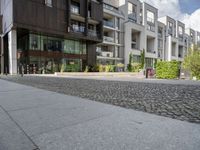 an asphalt street in front of apartment buildings and a bicycle path with cobblestone paved pavement