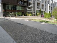 an asphalt street in front of apartment buildings and a bicycle path with cobblestone paved pavement