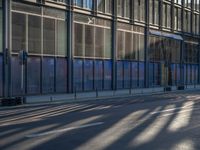 the sunlight reflects from several windows in a large building onto the street from outside the building