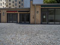 the sidewalk is paved with stones and has a bench in front of it, with no people inside