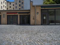 the sidewalk is paved with stones and has a bench in front of it, with no people inside