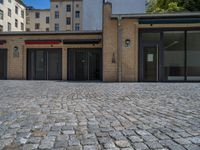 the sidewalk is paved with stones and has a bench in front of it, with no people inside