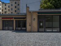 the sidewalk is paved with stones and has a bench in front of it, with no people inside