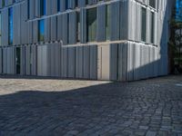 cobblestone driveway surrounded by modern buildings on sunny day with sun reflecting onto the windows