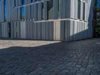 cobblestone driveway surrounded by modern buildings on sunny day with sun reflecting onto the windows