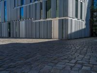 cobblestone driveway surrounded by modern buildings on sunny day with sun reflecting onto the windows