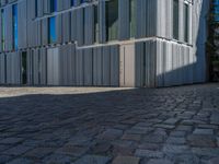 cobblestone driveway surrounded by modern buildings on sunny day with sun reflecting onto the windows