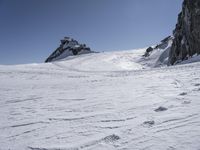 a person on skis stands on the snow by some rocks and mountains on a sunny day