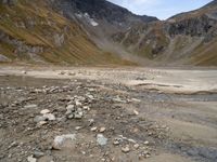 rocky area with mountains in the background, under a cloudy sky, and a stream