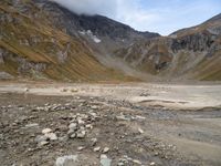 rocky area with mountains in the background, under a cloudy sky, and a stream