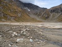 rocky area with mountains in the background, under a cloudy sky, and a stream