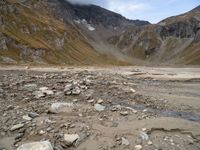 rocky area with mountains in the background, under a cloudy sky, and a stream