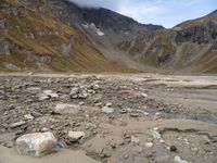 rocky area with mountains in the background, under a cloudy sky, and a stream