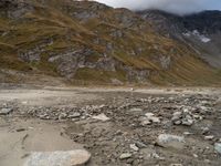 rocky area with mountains in the background, under a cloudy sky, and a stream