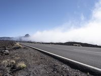 a road near the mountain side in the foggy sun day, and on the opposite bank are hills