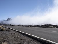 a road near the mountain side in the foggy sun day, and on the opposite bank are hills