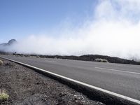 a road near the mountain side in the foggy sun day, and on the opposite bank are hills