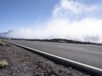 a road near the mountain side in the foggy sun day, and on the opposite bank are hills