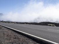 a road near the mountain side in the foggy sun day, and on the opposite bank are hills