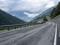 several cars traveling down the middle of the road under a cloudy sky in a mountain area