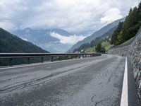 several cars traveling down the middle of the road under a cloudy sky in a mountain area