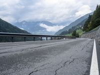 several cars traveling down the middle of the road under a cloudy sky in a mountain area