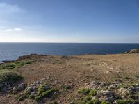 view from top of a hill looking at the ocean and rocks under a clear sky