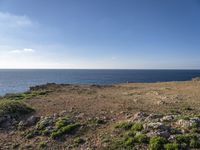 view from top of a hill looking at the ocean and rocks under a clear sky