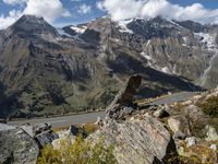 the view down a highway towards a valley with mountains and snow capped peaks behind it