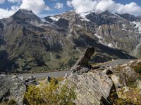 the view down a highway towards a valley with mountains and snow capped peaks behind it