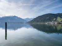 the lake is surrounded by mountains and a little boat out to sea and one small pole sticking out of the water