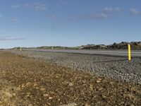 a paved road with gravel and rocks surrounding it in a barren, arid landscape on the horizon