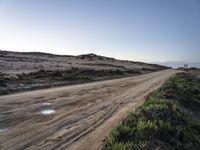 a dirt road that is covered with mud and grass near the ocean water on a clear day