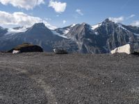 three mountain goats are resting on the ground by some boulders and snow capped mountains in the distance