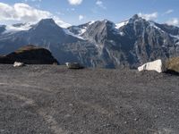 three mountain goats are resting on the ground by some boulders and snow capped mountains in the distance