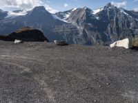 three mountain goats are resting on the ground by some boulders and snow capped mountains in the distance