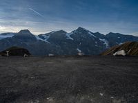 two people in tents are sitting at the bottom of a mountain on top of snow covered mountains