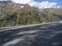 a man riding a motorcycle down a mountain road with mountains behind him behind him are trees