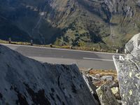 a person on a motorcycle riding down a road with mountains in the background and a highway winding in the distance