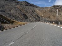 a motorcycle driving on the road between mountains and grass as a sign points to a right turn