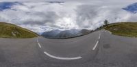 a panoramic photograph of a curved road with mountains in the background, with clouds in the sky