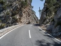 the highway has an old structure along it and tall steep cliffs behind it, making the curve a narrow