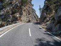 the highway has an old structure along it and tall steep cliffs behind it, making the curve a narrow