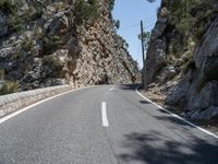 the highway has an old structure along it and tall steep cliffs behind it, making the curve a narrow