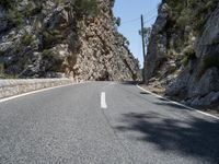 the highway has an old structure along it and tall steep cliffs behind it, making the curve a narrow