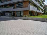 an open paved area with concrete walling, grass and a patio on one side