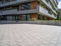 an open paved area with concrete walling, grass and a patio on one side